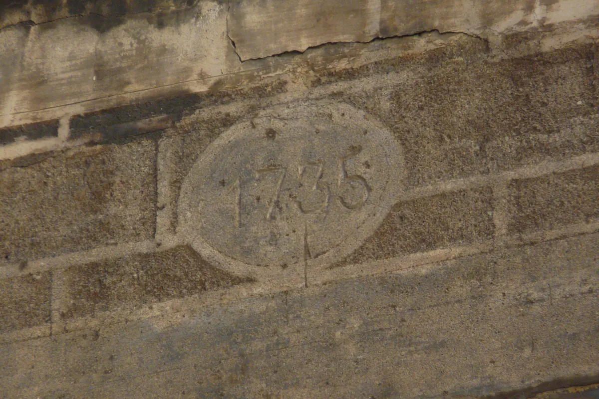 Um painel de pedra desgastado com a data 1735 gravada dentro de uma forma oval, encastrado numa parede na Carrer dels Abaixadors