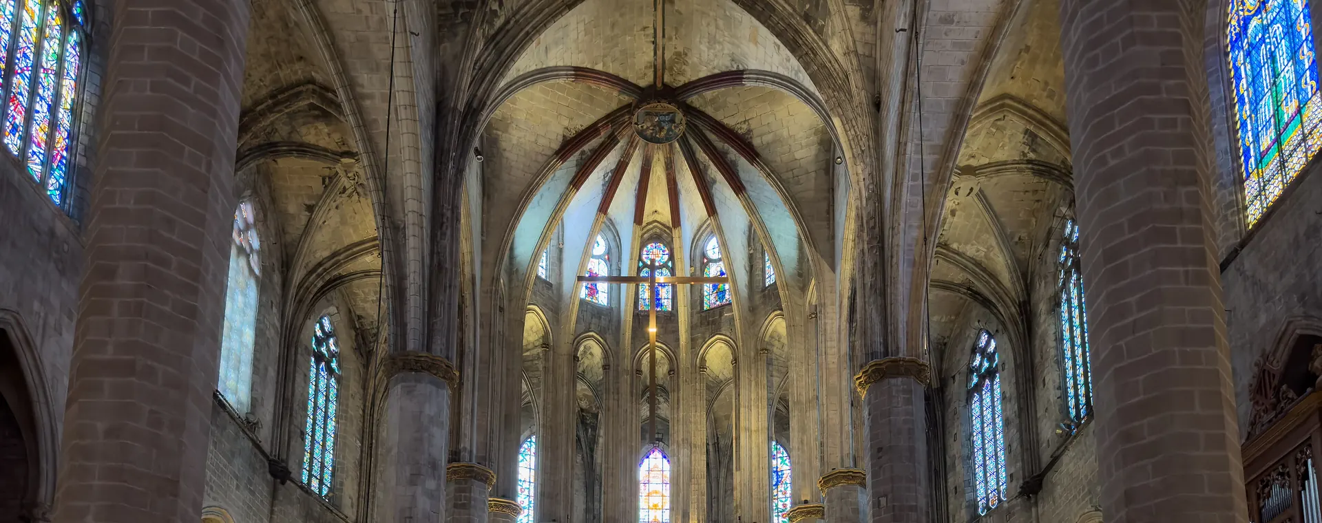 Uvnitř barcelonského kostela Santa Maria del Mar se štíhlé kamenné sloupy zvedají k žebrové klenbě a vitráže září zdola nasvícené