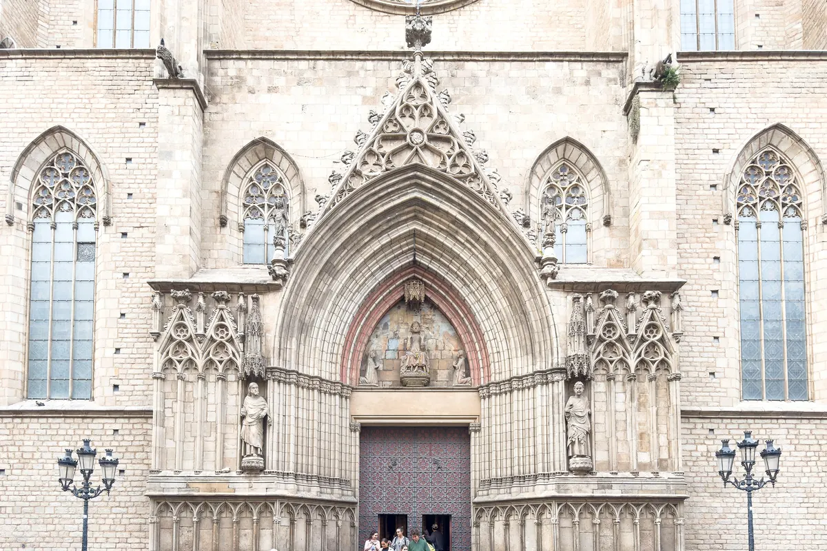 Západní portál Santa Maria del Mar – hrotitý gotický oblouk s vyřezávanými sochami a tmavými dřevěnými dveřmi